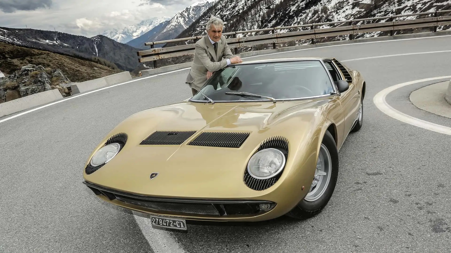 marcello gandini leaning against the roof of a lamborghini miura parked on a road.jpg
